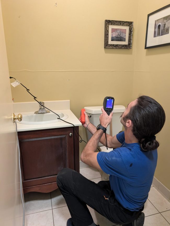 Technician using thermal imaging to inspect bathroom wall for water damage in Palm Beach County