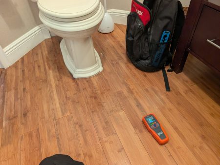 Moisture meter detecting water damage in wood flooring near toilet in Palm Beach County home