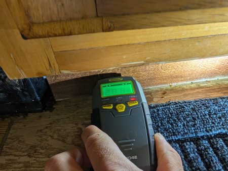 Moisture meter detecting water damage in wood flooring near cabinet base in Palm Beach County home