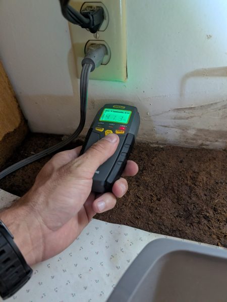 Moisture meter detecting elevated moisture behind wall near outlet after water damage in Palm Beach County